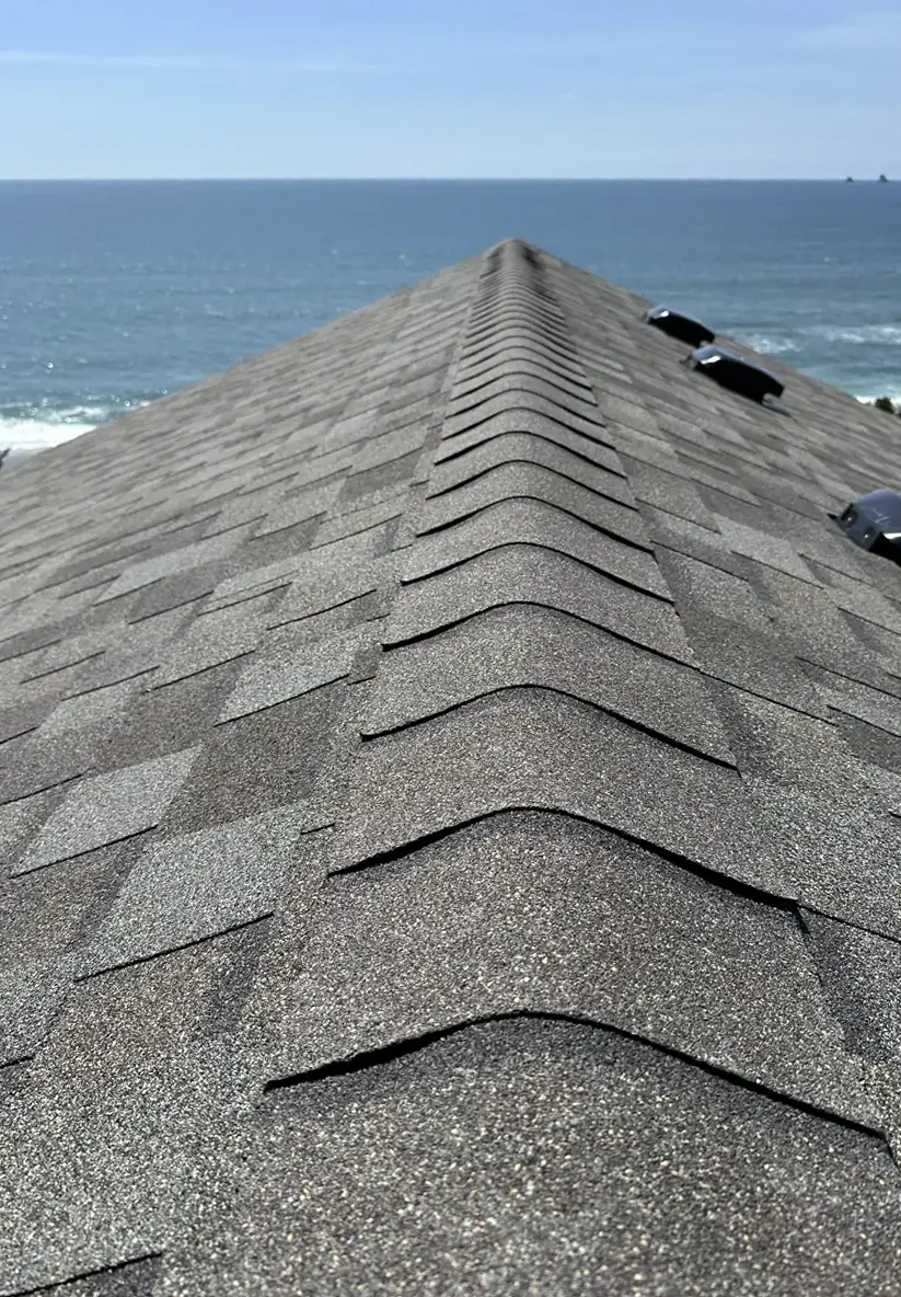A finished composition shingle roof ridge with the Pacific Ocean behind it